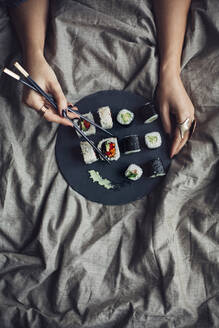 Frau isst Sushi mit Essstäbchen im Bett - BLEF14425