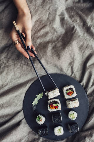 Hände einer Frau greifen nach einer Sushi-Platte auf dem Bett, lizenzfreies Stockfoto