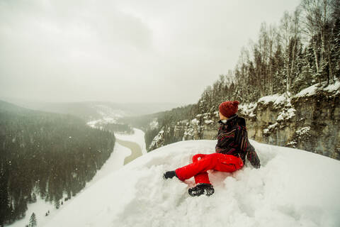 Kaukasischer Wanderer auf einer verschneiten Bergkuppe sitzend, lizenzfreies Stockfoto