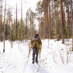 Mari man carrying snowshoes in snowy forest - BLEF14536