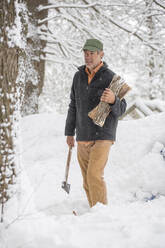 Mixed race man carrying firewood in snowy forest - BLEF14556