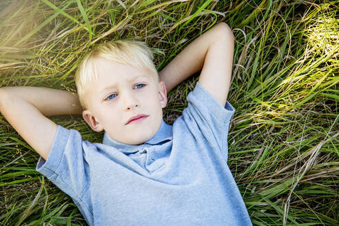 Ernster kaukasischer Junge, der im hohen Gras liegt - BLEF14626