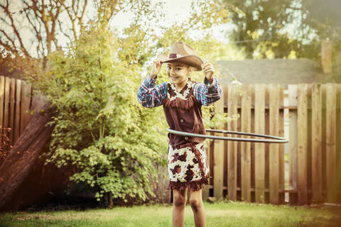 Mixed race girl in cowboy costume spinning plastic hoop in backyard stock photo