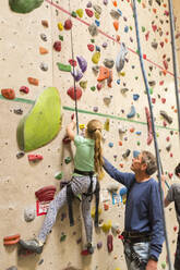 Caucasian father helping daughter climb rock wall indoors - BLEF14676