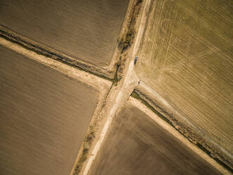 Aerial view of a car parked on a straight empty road in the middle of farmland in Estonia. - AAEF02022