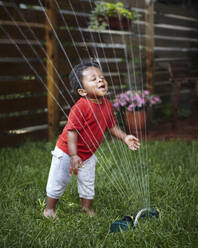 Afroamerikanisches Baby spielt im Rasensprenger - BLEF14697