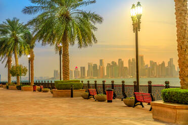 Bänke und Palmen entlang der Hafenpromenade in Porto Arabia at the Pearl-Qatar, mit beleuchteten Wolkenkratzern der West Bay Skyline zur blauen Stunde, Doha, Katar, Naher Osten - RHPLF00363