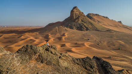 Aerial view of a girl on the top of a rocky mountain in the Camel Rock Desert Safari in UAE. - AAEF02247