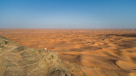 Aerial view of a girl on the top of a rocky mountain in the Camel Rock Desert Safari in UAE. - AAEF02248