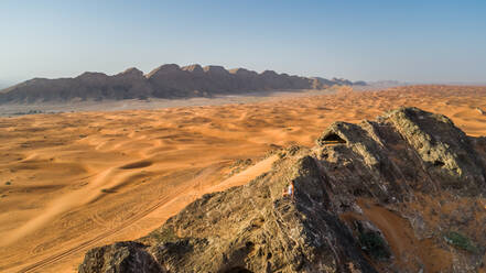Aerial view of a girl on the top of a rocky mountain in the Camel Rock Desert Safari in UAE. - AAEF02249