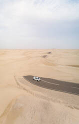 Luftaufnahme eines weißen Autos auf einer mit Sand bedeckten Straße in der Wüste, Abu Dhabi, VAE. - AAEF02346