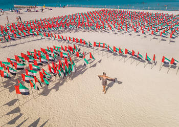 Luftaufnahme einer Frau inmitten von Nationalflaggen der Vereinigten Arabischen Emirate an einem Sandstrand in Dubai. - AAEF02447