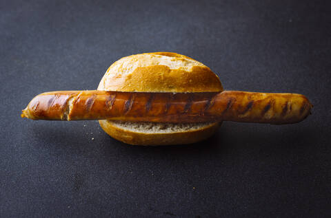 Gebratene Wurst im Brötchen isoliert auf dunklem Hintergrund, lizenzfreies Stockfoto