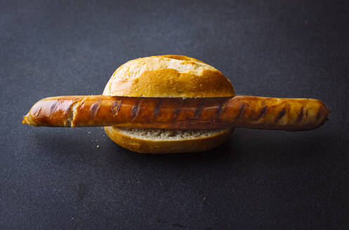 Roasted sausage in bread roll isolated on dark background - PPXF00234