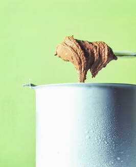 Chocolate ice cream in container during preparation against green background - PPXF00237