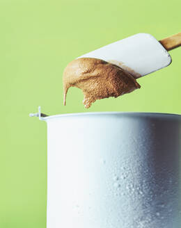 Close-up of chocolate ice cream on spatula over container against green background - PPXF00238