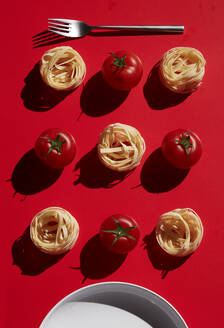Direkt über der Aufnahme von Nudeln mit Tomaten, die mit einer Gabel auf rotem Hintergrund angeordnet sind - KSWF02054