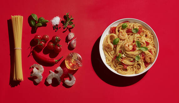 Shrimp pasta in bowl buy various ingredients on red background - KSWF02056