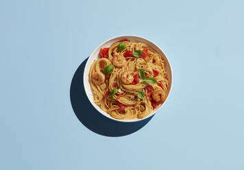 Directly above shot of shrimp pasta in bowl on blue background - KSWF02058