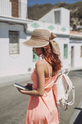 Modischer junger Tourist mit Buch und Rucksack auf der Straße stehend, Frigiliana, Malaga, Spanien - LJF00665