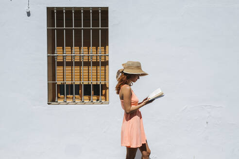 Rothaarige junge Frau liest ein Buch vor einem Haus, Frigiliana, Malaga, Spanien - LJF00675
