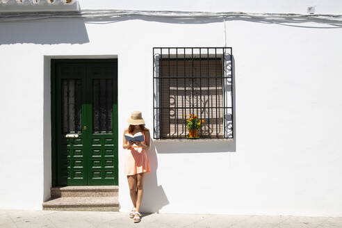 Rothaarige junge Frau liest ein Buch vor einem Haus, Frigiliana, Malaga, Spanien - LJF00679
