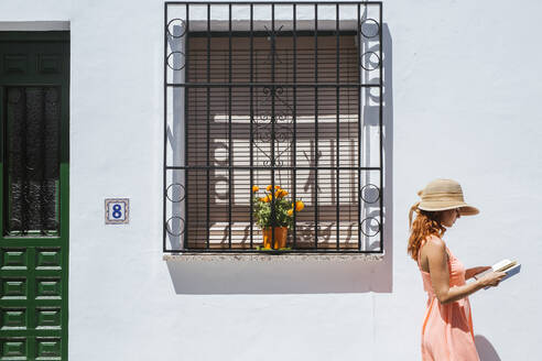 Rothaarige junge Frau liest ein Buch vor einem Haus, Frigiliana, Malaga, Spanien - LJF00681