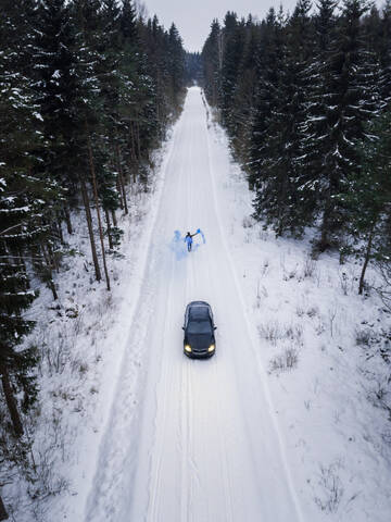 Luftaufnahme eines Mannes, der eine blaue Rauchgranate auf einer verschneiten Straße im Wald in Estland zündet., lizenzfreies Stockfoto