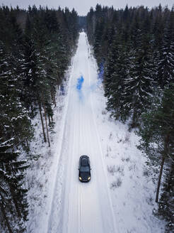 Luftaufnahme eines Mannes, der eine blaue Rauchgranate auf einer verschneiten Straße im Wald in Estland zündet. - AAEF02488