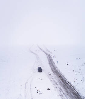 Luftaufnahme eines Autos auf einer vereisten Straße im Schneesturm in Rohukula, Estland. - AAEF02520