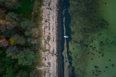 Luftaufnahme eines Bootes, das in der grünlichen Ostsee in der Nähe von Strand und Wald in Estland vertäut ist. - AAEF02688