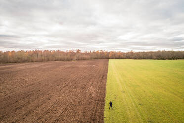 Luftaufnahme eines Mannes, der an der Grenze zwischen zwei verschiedenfarbigen Feldern in Estland steht. - AAEF02696