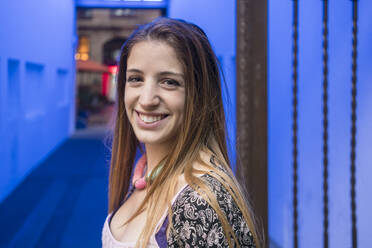 Porträt einer lächelnden jungen Frau mit blau beleuchtetem Hintergrund - TAMF02058