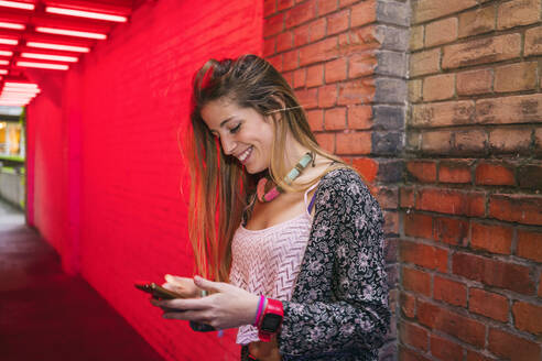 Glückliche junge Frau, die in der Stadt ein Mobiltelefon benutzt - TAMF02082