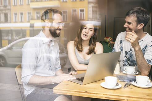 Eine Gruppe von Freunden sitzt mit einem Laptop in einem Café zusammen - TAMF02104