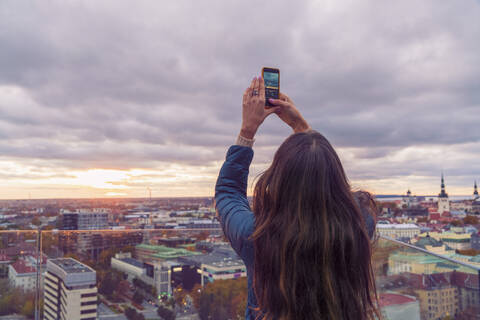 Frau, die mit ihrem Smartphone ein Foto von einer Aussichtsterrasse vor Sonnenuntergang macht, Tallinn, Estland, lizenzfreies Stockfoto