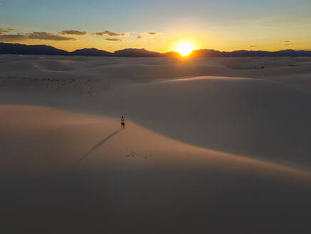 Luftaufnahme einer Person, die allein in der Mitte des White Sands National Monument bei Sonnenuntergang in Tularosa, USA, steht. - AAEF03013