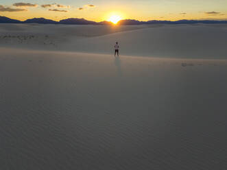 Luftaufnahme einer Person, die allein in der Mitte des White Sands National Monument bei Sonnenuntergang in Tularosa, USA, steht. - AAEF03016
