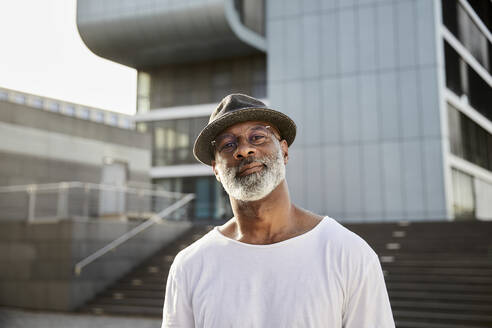 Portrait of smiling mature man with grey beard wearing hat in summer - FMKF05882