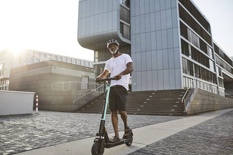 Lächelnder reifer Mann fährt E-Scooter im Sommer, lizenzfreies Stockfoto