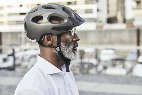Profil eines reifen Geschäftsmannes mit grauem Bart, der einen Fahrradhelm und eine Brille trägt, lizenzfreies Stockfoto
