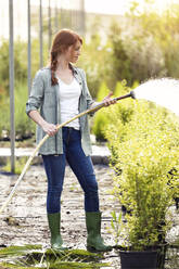 Junge Frau bewässert Pflanzen im Gewächshaus - JSRF00533