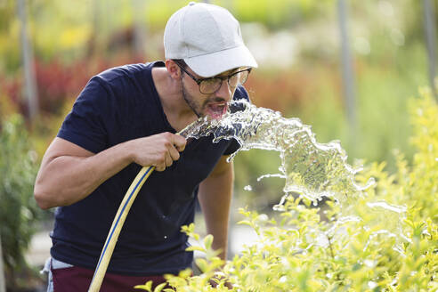 Young man drinking water from hose in the greenhous - JSRF00534