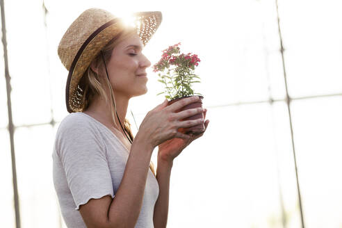 Beautiful young woman smelling at flower in the greenhouse - JSRF00548
