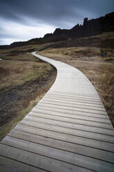 Boardwalk meandering towards rugged cliffs and stormy sky at Thingvellir National Park near Reykjavik, Iceland, Polar Regions - RHPLF00807