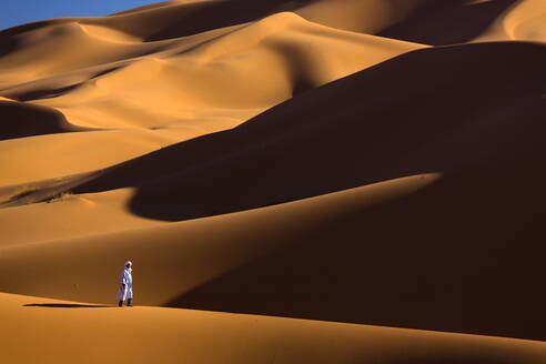 Berbermann, der zwischen den orangefarbenen Sanddünen des Erg Chebbi Sandmeeres spazieren geht, Sahara-Wüste bei Merzouga, Marokko, Nordafrika, Afrika - RHPLF00814