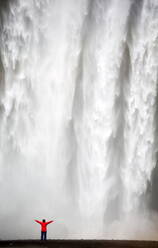 Frau in roter Jacke vor dem Wasserfall Skogafoss, Südisland, Island, Polarregionen - RHPLF00822