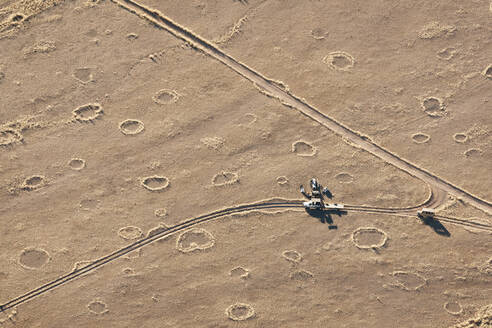 Luftaufnahme von Feenkreisen auf dem Boden, Straßen, Lastwagen und Männern, die das Frühstück in der Namib-Wüste aufbauen, Namibia, Afrika - RHPLF00934