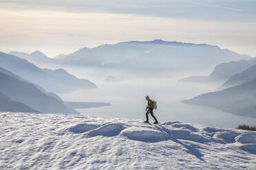 Winterlicher Blick auf den Comer See, während ein Wanderer mit Schneeschuhen voranschreitet, Vercana-Gebirge, Hoher Lario, Lombardei, Italien, Europa - RHPLF00985