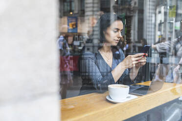 Business woman having a break in a cafe and working with laptop and smartphone - WPEF01798